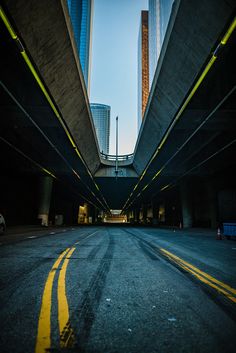 an empty street with yellow lines on the road and tall buildings in the background at dusk