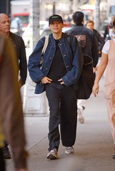 a man walking down the street wearing a denim jacket and black hat with his hands in his pockets