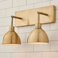 two light fixtures mounted on the wall in a room with white tile and brick walls