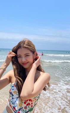 a young woman standing on top of a beach next to the ocean holding her hair