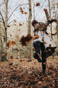 a woman is running through leaves in the woods with her arms up and head down