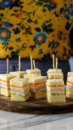 a person picking up sandwiches from a platter with toothpicks in it's hand