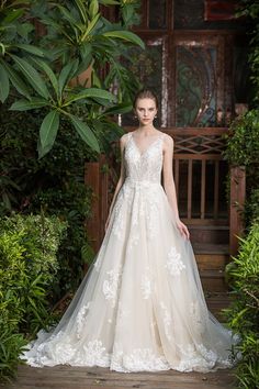 a woman in a wedding dress standing on a wooden platform with greenery behind her