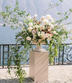 a vase filled with white flowers sitting on top of a stone floor next to a fence