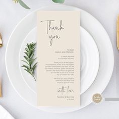 a place setting with white plates and silverware, gold cutlery and greenery