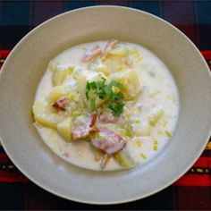 a white bowl filled with soup on top of a plaid table cloth next to a knife and fork