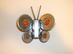 a metal clock with four orange buttons on it's face and two silver poles in the middle