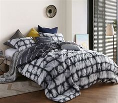 a bed with black and white comforter next to a window in a living room