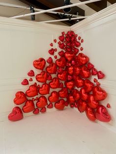 many red hearts are arranged in the shape of a triangle on a white wall and floor