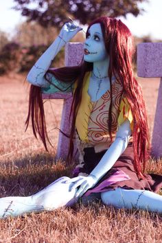 a woman with long red hair sitting on the ground next to a cross and tombstone