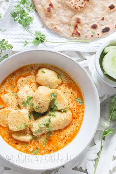 a white bowl filled with soup next to some pita bread and cucumber