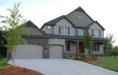 a large gray house with two garages and trees in the front yard, on a sunny day