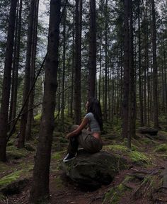 a person sitting on top of a rock in the woods next to some tall trees