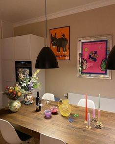 a wooden table topped with white chairs next to a vase filled with flowers and candles