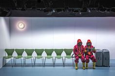 two people dressed in red and yellow sitting next to each other with luggage on the floor