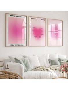 two pink posters hanging on the wall above a white couch with pillows and flowers in vases