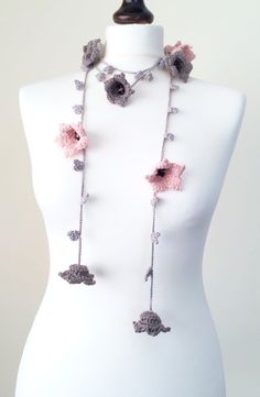 a white mannequin wearing a pink and gray crocheted necklace with flowers