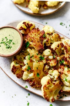 a white plate topped with cauliflower next to a bowl of ranch dressing