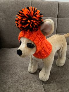 a white dog wearing an orange knitted hat and pom - pom on it's head