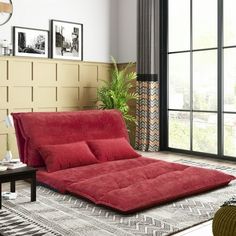 a red futon bed sitting on top of a rug in a living room next to a window