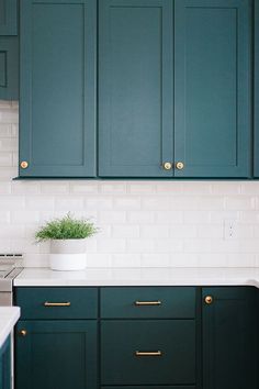 a kitchen with green cabinets and white tile backsplash, gold pulls on the cupboards