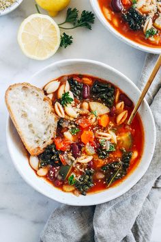 two bowls filled with soup next to lemons and bread on a white counter top