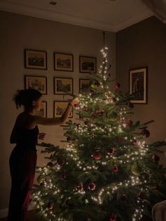 a woman decorating a christmas tree in her living room with lights on the top