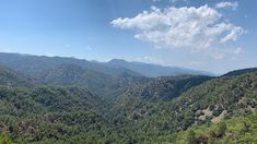 the mountains are covered in green trees and blue sky with white clouds above them, as seen from an overlook point on a sunny day