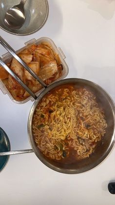 two pans filled with food sitting on top of a table next to bowls and spoons