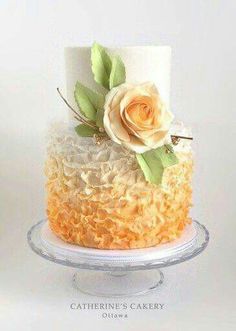 a three tiered cake with white and orange frosting, topped with a single rose