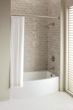 a bath tub sitting under a window next to a shower curtain in a white bathroom