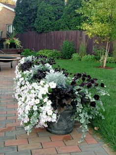 a large potted planter filled with purple and white flowers on a brick walkway