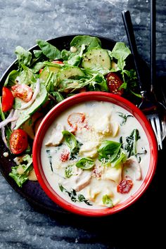 a red bowl filled with soup next to a salad on top of a black plate