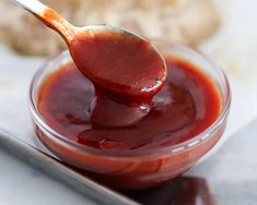 a spoon full of ketchup sitting on top of a glass bowl filled with sauce