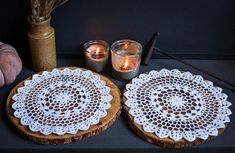 two wooden coasters with lace doily sit on a table next to some candles