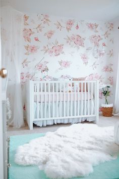 a baby's room with pink flowers on the wall and white rugs in front of the crib