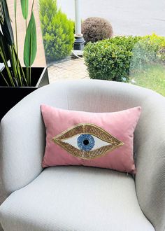 a pink pillow with an eye on it sitting in a chair next to a potted plant