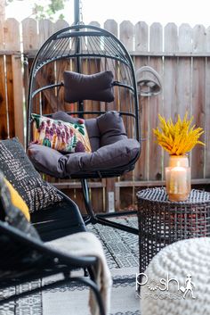 a chair and table on a patio with flowers in the vase, next to a birdcage