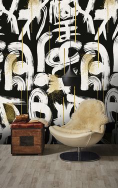 a white chair sitting in front of a wall with black and gold designs on it