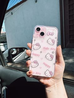 a person holding up a pink hello kitty phone case in their left hand, while sitting in a car