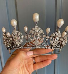 a hand holding a tiara with pearls and diamonds on it's headpiece