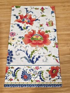 a white table cloth with red and blue flowers on it sitting on top of a wooden floor