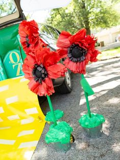 some red flowers are sitting on the ground next to a green pole and yellow trash can