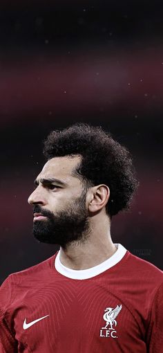 a man with a beard wearing a red shirt and standing in front of a soccer field