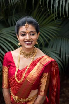 a woman in a red and gold sari smiles at the camera with palm trees behind her