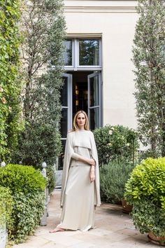 a woman standing in front of a building wearing a long beige dress and cape over her shoulders