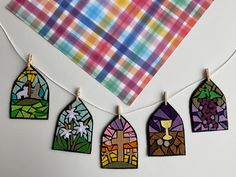 colorful stained glass houses hanging from clothes pins on a white surface with a plaid napkin in the background