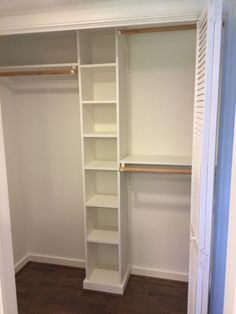 an empty walk in closet with white shelving and wood flooring on the side