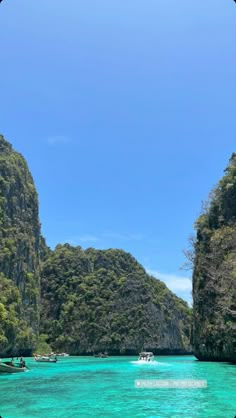 boats floating on the water near mountains and trees in the ocean with clear blue skies