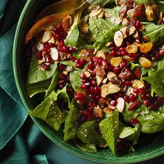 a green bowl filled with spinach and pomegranates on top of a table